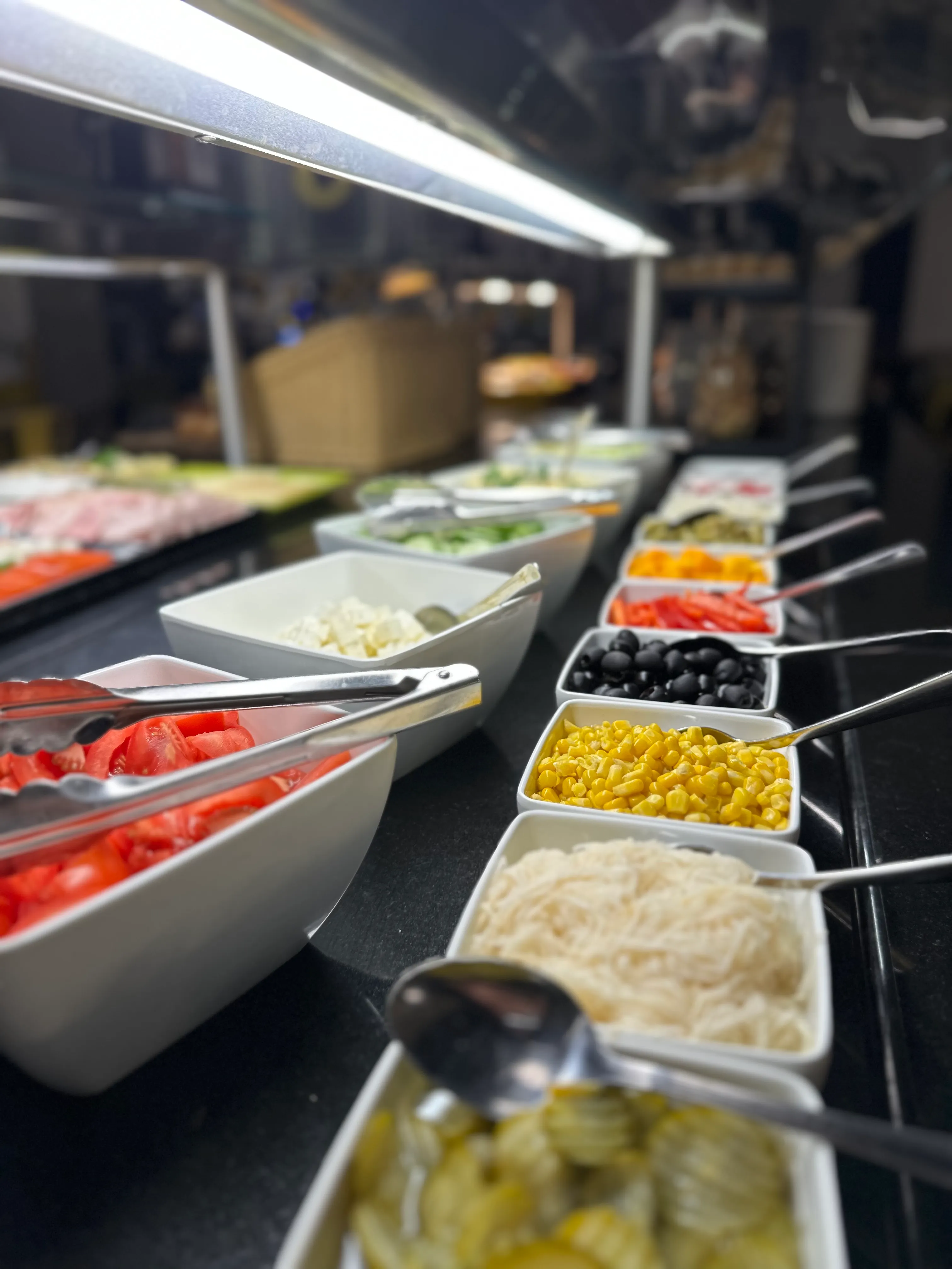 Bufet śniadaniowy w restauracji o3eat — świeże warzywa, sery i dodatki w podświetlanej ladzie