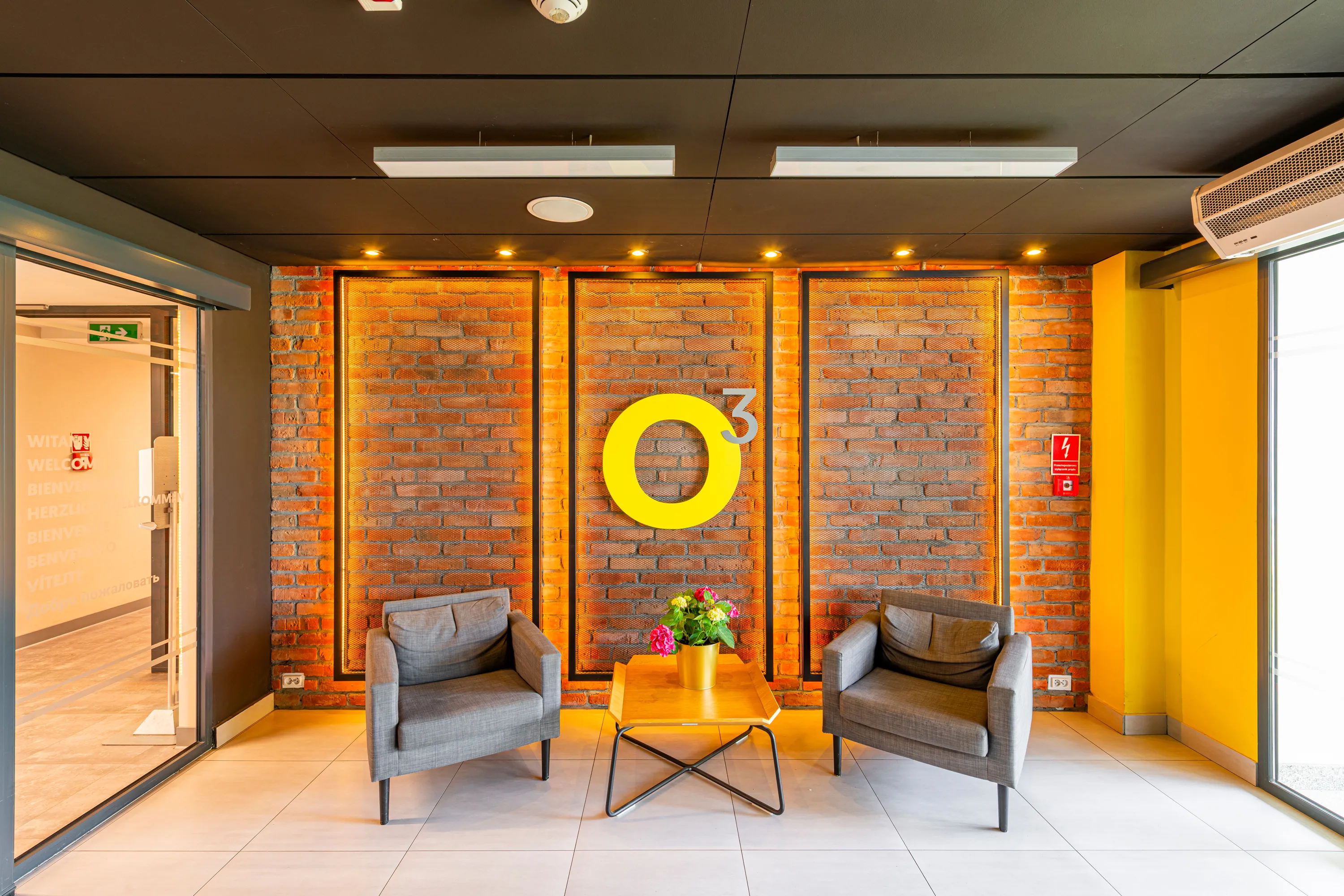 Strefa wejściowa o3Hotel — fotele na tle ceglanej ściany z żółtym logo o3